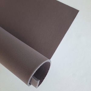 Könnte beinhalten: Nahaufnahme eines zusammengerollten Stücks braunen Stoffes. Der Stoff ist strukturiert und hat einen leichten Glanz. Das Wort "pepper" ist in schwarzer Schrift unter dem Stoff geschrieben.