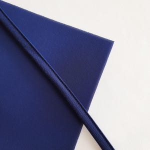 May include: A close-up of a dark blue fabric with a contrasting dark blue trim. The fabric is folded in half, creating a diagonal line.