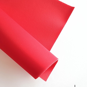 Könnte beinhalten: Nahaufnahme einer leuchtend roten Filzplatte, die in der Mitte gefaltet ist, mit dem Wort "rot" darunter.