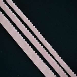 May include: Three strips of pink elastic with scalloped edges against a black background.