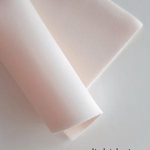 Könnte beinhalten: Nahaufnahme eines hellbeigen Stoffes. Der Stoff ist in der Mitte gefaltet und die Kanten sind sichtbar. Der Stoff ist glatt und hat eine weiche Textur.