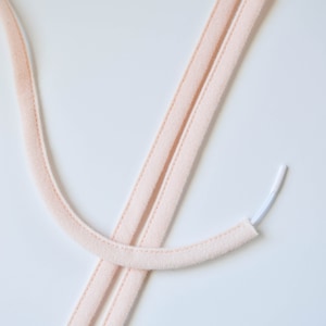 May include: Two strands of pale pink elastic cord with a white elastic cord attached to one end.