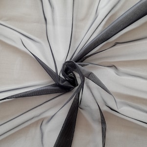 Puede incluir: Tela de tul negro transparente con una textura de malla fina. La tela está drapeada y doblada, creando un aspecto suave y fluido.