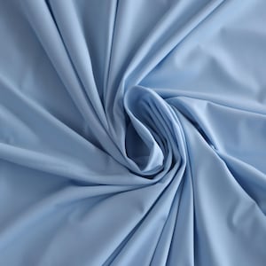Könnte beinhalten: Nahaufnahme eines hellblauen Stoffes mit glatter Textur. Der Stoff ist gefaltet und drapiert und erzeugt einen weichen und fließenden Look.