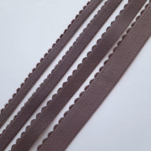 May include: Close-up of several strips of brown decorative trim with a scalloped edge. The trim appears to be made of a textured material, and the strips are arranged diagonally across a white background.