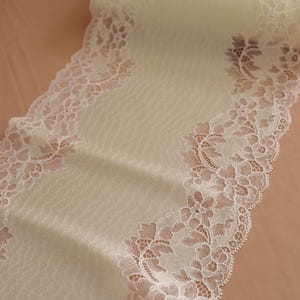 Puede incluir: Borde de encaje blanco con un delicado patrón floral sobre un fondo verde claro.