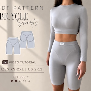 Peut inclure: Un patron PDF pour short de cyclisme comprenant un haut court à manches longues gris clair et un short taille haute assorti. L'image contient le texte : PDF PATTERN BICYCLE SHORTS, VIDEO TUTORIAL, SIZES XS-2XL | US 2-12, et DIFFICULTY.