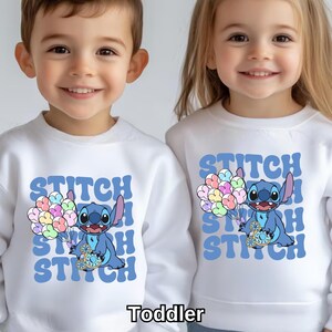 May include: Two white toddler sweatshirts with a blue Stitch character holding balloons. The text "Stitch" is repeated in a retro font on each shirt.