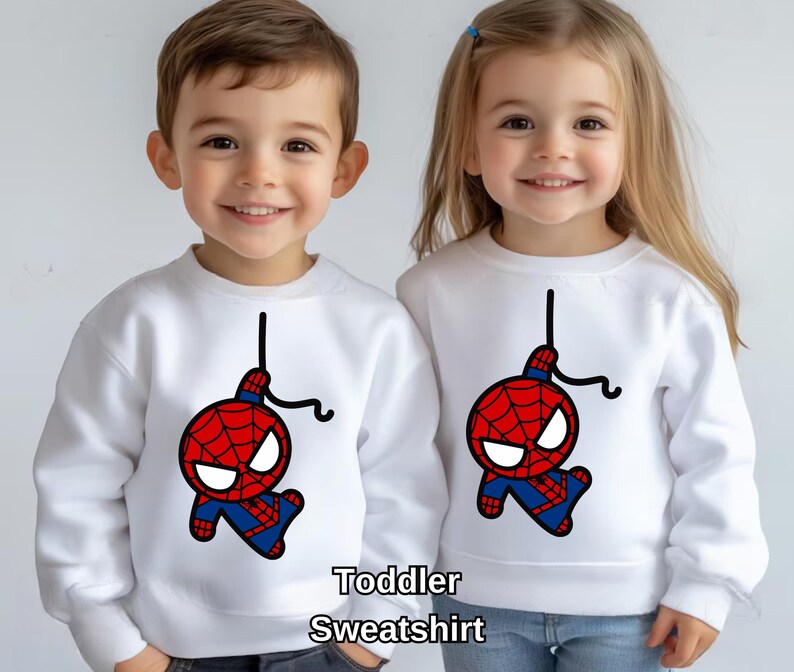 Puede incluir: Dos sudaderas blancas para ni&ntilde;os peque&ntilde;os con una imagen de dibujos animados de Spiderman colgando boca abajo. El texto "Toddler Sweatshirt" est&aacute; impreso debajo de la imagen.