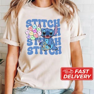 May include: A beige t-shirt with a blue Stitch character holding a blue and white balloon. The text "Stitch Stitch Stitch" is printed in blue on the shirt.