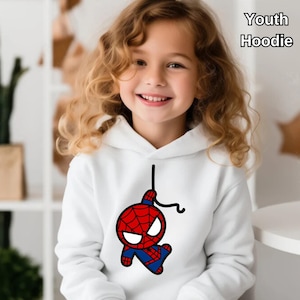 Puede incluir: Sudadera blanca para j&oacute;venes con una imagen de dibujos animados de Spiderman colgando de una telara&ntilde;a. La sudadera tiene una capucha con cord&oacute;n.