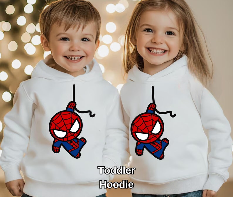 Puede incluir: Dos ni&ntilde;os con sudaderas blancas con una imagen de dibujos animados de Spiderman colgando boca abajo. Las sudaderas dicen "Toddler Hoodie" en la parte inferior.