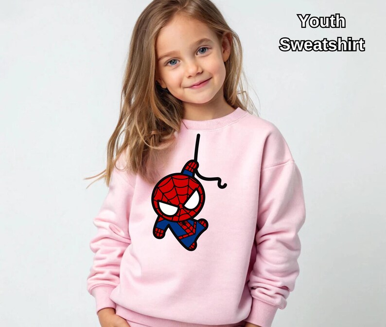 Puede incluir: Sudadera rosa para j&oacute;venes con una imagen de dibujos animados de Spiderman colgando de una telara&ntilde;a. El texto "Youth Sweatshirt" est&aacute; en la esquina superior derecha de la imagen.