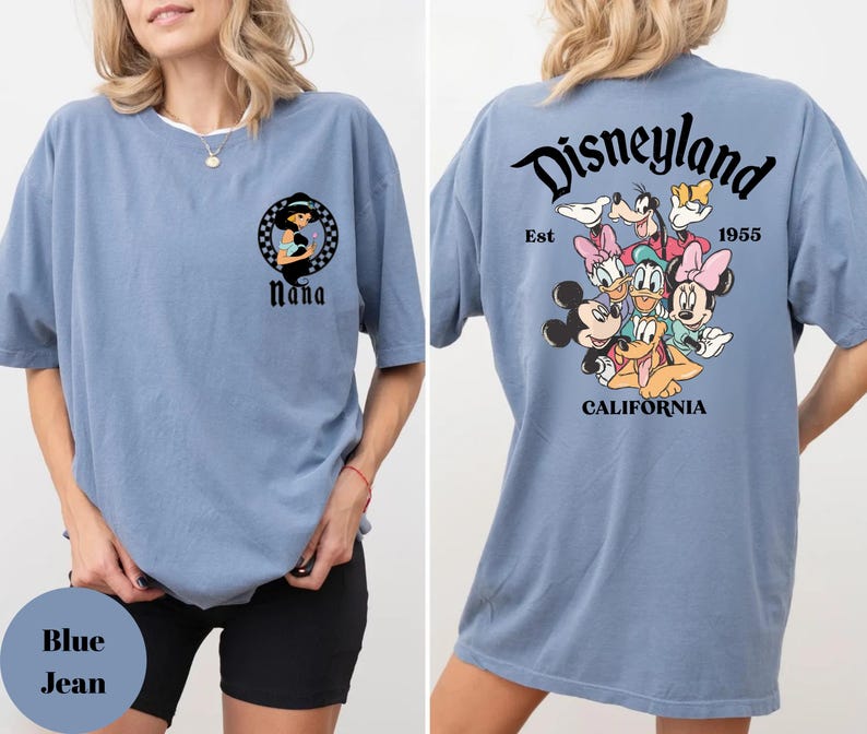 May include: A blue jean colored t-shirt featuring a front graphic of a woman in a black and white circular design with the word "Nana" below. The back of the shirt has a Disneyland graphic with cartoon characters and the text "Disneyland California 1955".