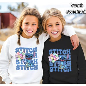 May include: Two children wearing matching white and black youth sweatshirts with a blue Stitch character holding balloons and the text "Stitch" repeated in a retro font.