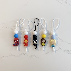 May include: Five colourful beaded keychains with different cartoon character charms. The charms include Spiderman, Iron Man, Batman, Belle, and Elsa.