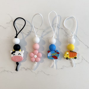 May include: Four colourful silicone teethers with different animal and vehicle designs. Each teether has a white bead and a black bead. The teethers are attached to white cords.