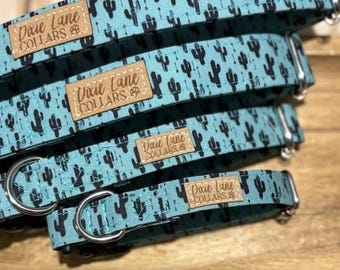 May include: A stack of dog collars with a teal background and a black cactus pattern. Each collar has a metal D-ring and a brown leather patch that reads "Dixie Lane Collars".