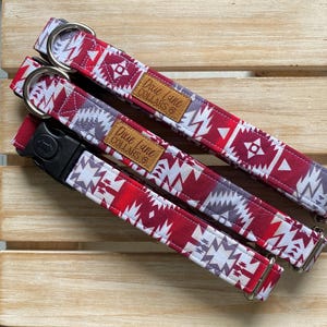 Peut inclure: Deux colliers pour chien à motifs rouge, blanc et gris avec des accessoires en argent et une étiquette en cuir marron qui dit "Dove Lane Collars".