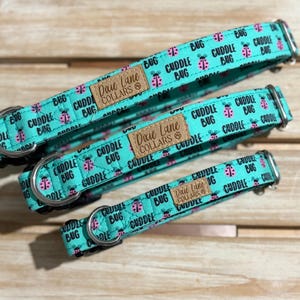 Puede incluir: Tres collares para perros de diferentes tamaños. Los collares turquesa presentan un patrón repetido de mariquitas rosas y las palabras "Cuddle Bug". Cada collar tiene una etiqueta de cuero marrón con "Dixie Lane Collars".