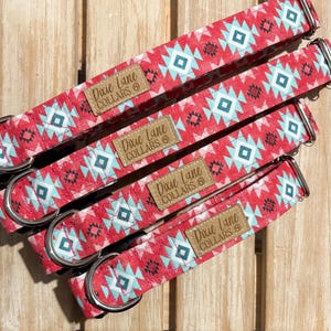 Puede incluir: Cuatro collares rojos para perros con un patrón geométrico en turquesa y blanco. Cada collar tiene una anilla en D de metal y una etiqueta de cuero marrón que dice "Dixie Lane COLLARS". Los collares están dispuestos en diagonal sobre una superficie de madera.