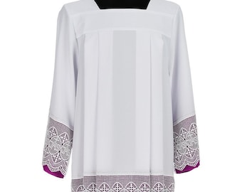 May include: White liturgical alb with a square neckline and long sleeves. The sleeves and hem are trimmed with white lace over a purple fabric. The lace features a repeating pattern with the letters IHS and crosses.