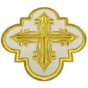 May include: A white fabric patch with a gold embroidered cross. The cross has a decorative design with swirls and flourishes.
