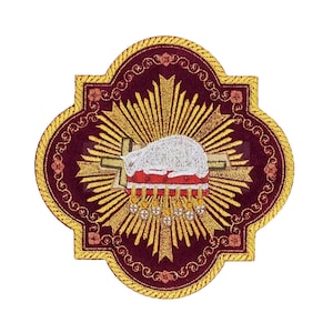 以下が含まれることがあります： 金色の刺繍が施された、濃い赤紫色のベルベットのパッチ。デザインは、赤い十字架の上に横たわる子羊と、その背後に輝く金色の太陽の光を表現しています。