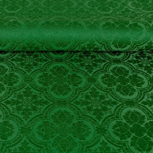 Op de afbeelding: Groene stof met een herhalend patroon van gestileerde bloemen en bladeren. De stof heeft een textuur, bijna fluweelachtig.