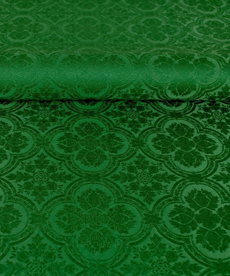 Op de afbeelding: Groene stof met een herhalend patroon van gestileerde bloemen en bladeren. De stof heeft een textuur, bijna fluweelachtig.