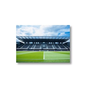 Könnte beinhalten: Ein Fußballstadion mit grünem Rasen und schwarzen Sitzen. Der Himmel ist blau mit Wolken. Das Stadion hat eine große Dachkonstruktion. Die Perspektive ist von unten.