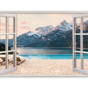 Puede incluir: Un cuadro de pared que muestra un marco de ventana abierto con vistas a un patio de piedra con dos tumbonas, una piscina infinita de color turquesa y un gran lago rodeado de picos montañosos nevados bajo un suave cielo al atardecer.