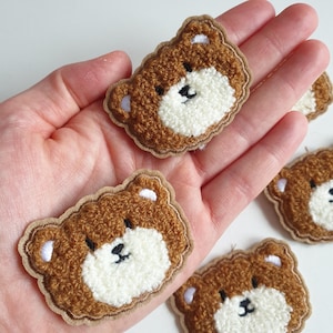 May include: Five brown fuzzy bear face patches with white fur around the nose and mouth. The patches are sewn with brown thread around the edges.