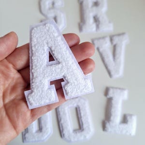 May include: White felt letters in the alphabet, including the letters A, R, V, O, and L. The letters are thick and have a fuzzy texture.