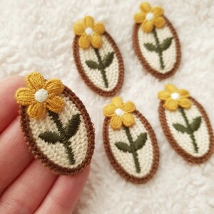 May include: Five embroidered iron-on patches featuring a yellow flower with a white center and green stem in a brown oval frame.