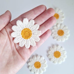 May include: Five crocheted white daisy flowers with yellow centres. The flowers are approximately 5 cm in diameter.