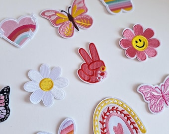 May include: Assortment of colorful iron-on patches featuring various designs, including butterflies, flowers, a peace sign, a rainbow, and a heart.