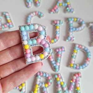 May include: A close-up of a letter B made of colourful beads. The letter is surrounded by other letters of the alphabet, all made of beads.