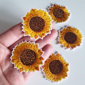 May include: Embroidered sunflower patches with yellow petals, brown centres, and white scalloped edges. The patches are in various sizes and are ideal for adding to clothing, bags, or other craft projects. The sunflowers are a bright and cheerful design.
