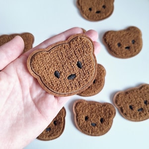 May include: A set of seven brown fuzzy bear-shaped patches with black embroidered eyes and noses.