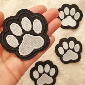 May include: Black and white paw print patches. The patches have a black outline with white embroidered paw pads. These patches are a cute accessory for clothing, bags, or other fabric items. A fun way to show your love for pets.