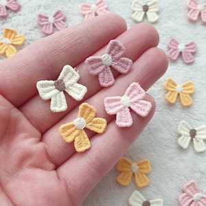 May include: Assortment of small fabric bows in pink, white and yellow with a white centre. The bows are perfect for adding a touch of whimsy to crafts, clothing and accessories.