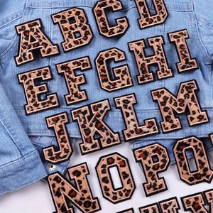 May include: A set of iron-on alphabet patches in a leopard print design. The patches are in uppercase letters and are ideal for adding a personalised touch to clothing, bags, or other fabric items.
