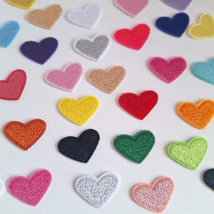 Könnte beinhalten: Sortiment an Filz-Herz-Patches in verschiedenen Farben, darunter Rot, Rosa, Blau, Grün, Gelb, Orange und Weiß. Die Herzen sind alle gleich groß und gleich geformt und in einem zufälligen Muster angeordnet.