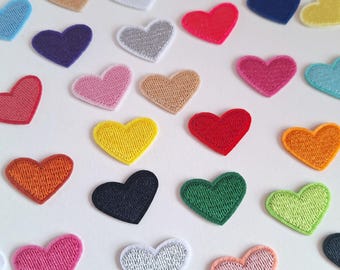 May include: Assortment of felt heart patches in various colors, including red, pink, blue, green, yellow, orange, and white. The hearts are all the same size and shape, and they are arranged in a random pattern.