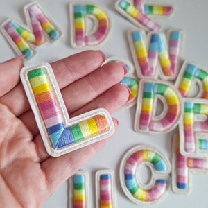 May include: A set of colourful embroidered felt letters in rainbow colours. The letters are on a white background and are arranged in a random order. The letters are all uppercase and are about 2 inches tall.