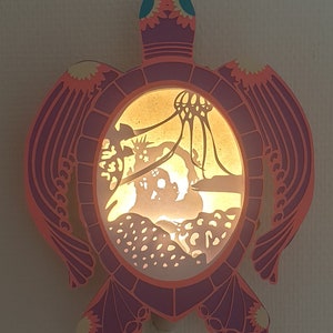 luminaire lightbox dans cadre en forme de tortue rose réalisé intégralement à la main en papier et carton pour décoration murale sur la mer