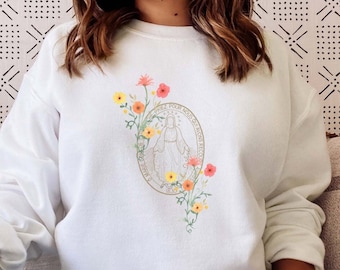 May include: A white sweatshirt with a floral design featuring a woman in a circle. The flowers are in shades of pink, yellow, and orange.