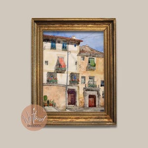 May include: A watercolour painting of a building with a red door and a balcony. The building is painted in shades of yellow, white, and brown. The painting is framed in a gold frame.