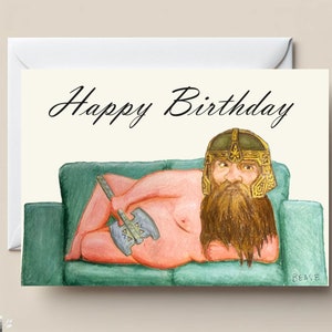 May include: A humorous birthday card featuring a cartoon illustration of a naked, bearded man wearing a helmet and holding an axe, relaxing on a green sofa. The card reads "Happy Birthday".
